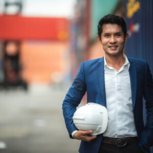 An engineer holding a hard hat at a shipping container yard